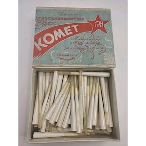 May include: An open box of vintage Komet brand paper cigarette tips. The box is light blue with red and white text and graphics. The tips are white with a clear, tapered tube.
