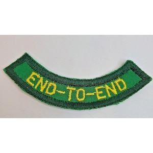 May include: A curved, embroidered patch featuring a bright green background with a dark green border. The text END-TO-END is stitched in yellow thread across the center of the patch. The design is shaped like an arc with a flat top and bottom.