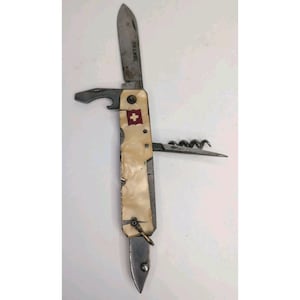 May include: A multi-tool pocket knife with an off-white pearlescent handle featuring a red and white Swiss cross emblem. The knife includes a main blade, a bottle opener, a corkscrew, and a small secondary blade, with a metal ring at the base.