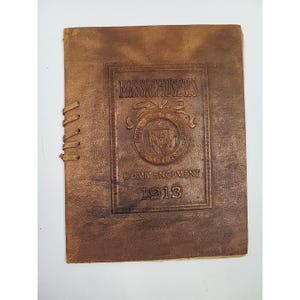 Könnte beinhalten: Ein Vintage-Broschüre aus braunem Leder mit dem geprägten Text "MASSACHUSETTS COMMENCEMENT 1913" und einem Siegel. Die Broschüre ist mit einem genähten Rücken gebunden. Das Leder hat ein abgenutztes, gealtertes Aussehen.
