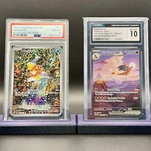 May include: Two graded Pokémon trading cards. The left card features Magikarp, and the right card showcases Charizard ex. Both cards are encased in protective holders and displayed on purple stands. The Charizard card is graded a 10.