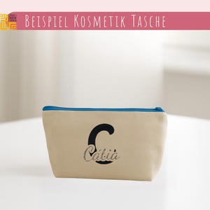 May include: A beige cosmetic bag with a blue zipper and the name "Catia" in a cursive font with a black "C" initial. The bag has the text "BEISPIEL KOSMETIK TASCHE" in a pink banner.