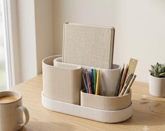 May include: A multi-compartment desk organizer with a ribbed texture in shades of beige and white. The organizer holds a beige fabric-covered notebook, several colorful pens, and a wooden ruler. The base is oval-shaped with vertical ridges.