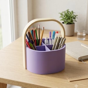 Pode incluir: Um organizador de mesa redondo na cor lavanda com uma alça de madeira clara e quatro compartimentos internos. O organizador está cheio de vários lápis de cor, marcadores e canetas. A estrutura é feita de material sólido com acabamento liso.