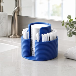 Può includere: Un organizer da bagno in plastica blu con un design esterno a coste. Lo scomparto cilindrico centrale contiene una pila di dischetti di cotone bianchi, mentre i compartimenti laterali curvi circostanti contengono bastoncini di cotone bianchi.
