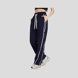 May include: Navy blue sweatpants with white side stripes and a drawstring waist. The pants have pockets and are paired with white sneakers. A casual and sporty look.