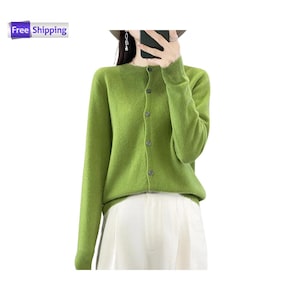Può includere: Un cardigan verde chiaro con scollo tondo e maniche lunghe. Il maglione con bottoni è abbinato a pantaloni bianchi. Il cardigan è in tinta unita e sembra essere realizzato in un materiale morbido.