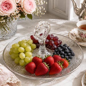 Könnte beinhalten: Ein Serviertablett aus klarem Glas mit einem dekorativen Mittelgriff und einer strukturierten Oberfläche. Das Tablett ist mit frischen grünen Trauben, roten Trauben, Blaubeeren und Erdbeeren gefüllt, die in Abschnitten um den Griff angeordnet sind.