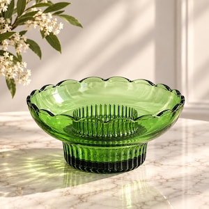 Peut inclure: Un bol en verre vert translucide doté d'un bord festonné et d'un pique-fleurs intégré au centre avec des tiges verticales. La base du bol présente un design cylindrique cannelé, offrant une assise stable à ce récipient en verre décoratif.
