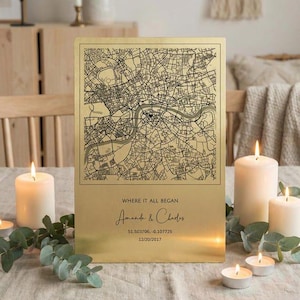 May include: A rectangular gold-colored metal plaque featuring a black street map print with a small heart icon. The text reads: WHERE IT ALL BEGAN, Amanda & Charles, 51.503706, -0.107725, and 12/20/2017. The plaque has a smooth, reflective finish.