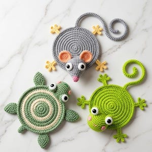 May include: Three handmade crochet animal coasters: a gray mouse with pink ears and nose, a green turtle, and a green frog. Each coaster features a spiral design and is embellished with small details like eyes and feet.