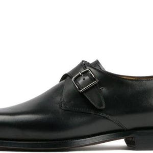 May include: A single black leather monk strap shoe with a silver buckle. The shoe has a pointed toe and a low heel. The leather appears smooth and polished, suggesting a formal or dressy style. The shoe is designed for a right foot.