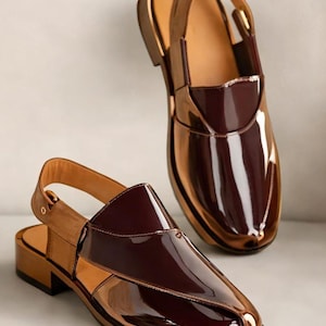 May include: A pair of glossy, two-tone shoes with a slingback design. The shoes feature a rich burgundy vamp and a metallic bronze-coloured body. The soles are a dark brown, and the shoes have a low heel.