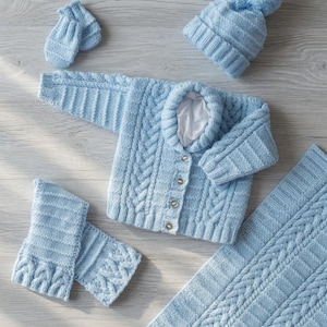 Può includere: Un set per neonati azzurro chiaro, composto da cardigan, cappello, guanti e coperta. Il cardigan presenta un motivo a trecce e chiusura con bottoni. Il set è progettato per bambini di 30.5-56 cm. Il testo "Digital Knitting Pattern" è visibile.