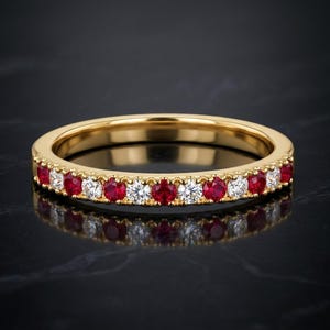 Peut inclure: Une bague en or jaune ornée d'une alternance de rubis rouges et de diamants blancs ronds sertis sur la moitié avant de l'anneau. Le métal présente une finition polie et les pierres sont maintenues par de petites griffes métalliques.