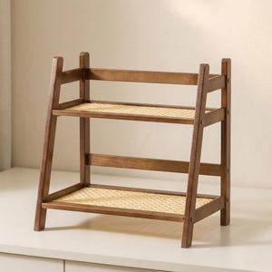 Puede incluir: Una estanter&iacute;a de madera de dos niveles con un acabado marr&oacute;n c&aacute;lido. Los estantes est&aacute;n hechos de material tejido de color claro. El marco tiene un dise&ntilde;o similar a una escalera, con patas en &aacute;ngulo y soportes horizontales. La estanter&iacute;a est&aacute; dise&ntilde;ada para exhibici&oacute;n o almacenamiento.