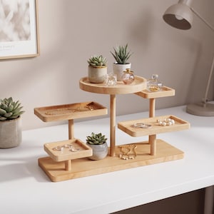 May include: A multi-tiered wooden jewelry organizer with various small trays and platforms. The organizer holds necklaces, bracelets, rings, and small potted succulents. The natural wood finish complements the jewelry and plants, creating a decorative display.