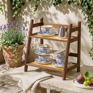 Puede incluir: Una estanter&iacute;a de madera de dos niveles exhibe tazas y platillos azules y blancos. Una jarra de acero inoxidable se encuentra en el estante superior. La estanter&iacute;a est&aacute; sobre una superficie de piedra, con una planta de lavanda en maceta y fruta en el fondo.