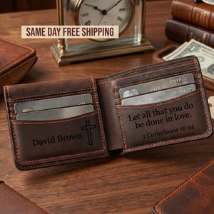 May include: Open brown leather wallet with orange stitching. The wallet is open, revealing card slots and a compartment with the text "Let all that you do be done in love. 1 Corinthians 16:14". The name "David Brown" and a cross are also visible.