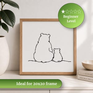 May include: A framed cross-stitch design featuring a mother bear and cub in black thread on a white background. The wooden frame surrounds the artwork. The image includes a green circle with the text "Beginner Level". The text "Ideal for 20x20 frame" is also present.