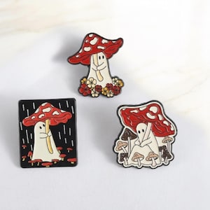 Può includere: Tre spille smaltate a tema fungo. Ogni spilla presenta un cappello di fungo rosso e bianco a pois. Una spilla ha un fungo con una faccia e dei fiori. Un'altra è un fungo con una figura spettrale su sfondo nero.