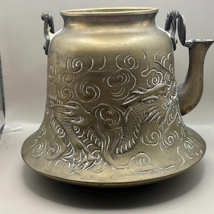 May include: Antique brass teapot with dragon and cloud relief carvings. The teapot has a wide base, a bell-shaped body, and a curved spout. Two handles are attached to the top. The dragon design is highlighted with white accents.