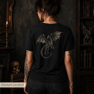 May include: A black short-sleeve t-shirt featuring a detailed graphic print of a dragon with spread wings on the back. The dragon is depicted in shades of grey and muted green, shown in a flying position with its tail curved downward.