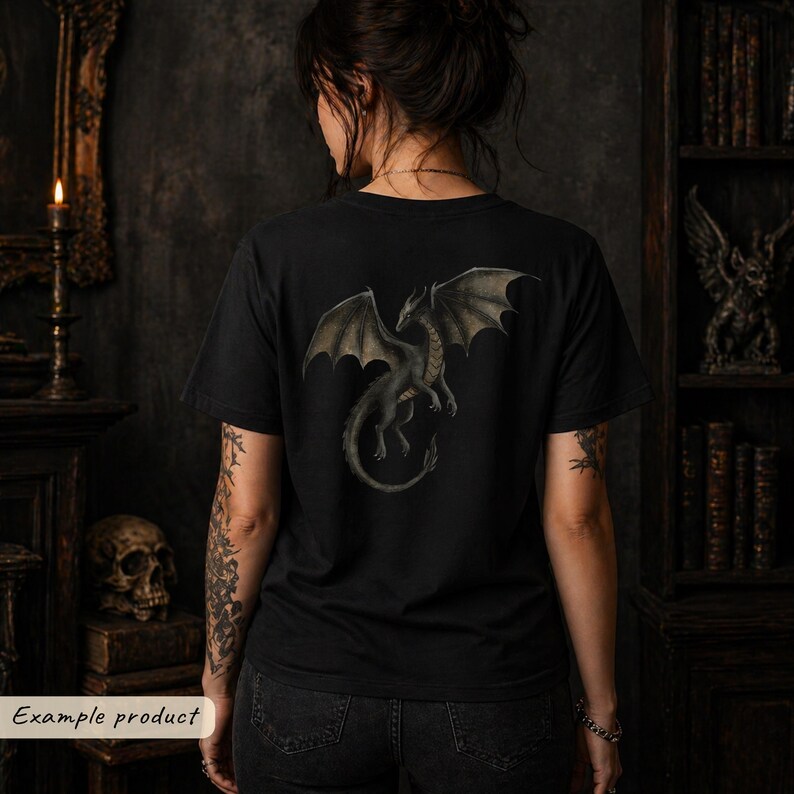 May include: A black short-sleeve t-shirt featuring a detailed graphic print of a dragon with spread wings on the back. The dragon is depicted in shades of grey and muted green, shown in a flying position with its tail curved downward.