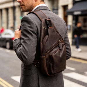 Puede incluir: Bandolera de cuero marrón oscuro con múltiples compartimentos con cremallera y una correa para el hombro. La bolsa se lleva cruzada. El cuero tiene un aspecto envejecido.