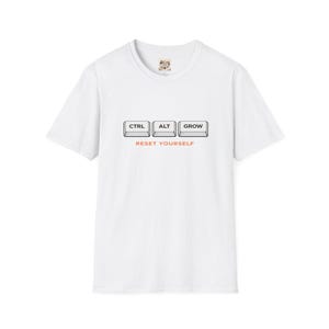 May include: White t-shirt with a crew neck featuring the words "CTRL", "ALT", and "GROW" in a keyboard key design. Below the keys, the text "RESET YOURSELF" is printed in orange. The shirt is a casual wear item.