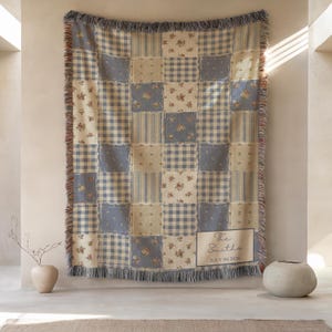 May include: A patchwork throw blanket with a mix of floral, gingham, and striped patterns in blue, beige, and white. The blanket has a fringed edge and a rectangular label with the text "The Smiths" and "JULY 04 2026".