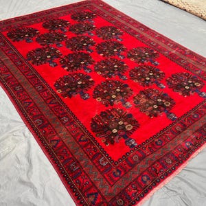 May include: A rectangular red rug with a repeating floral pattern. The rug has a dark border with intricate geometric designs. The central field features multiple floral bouquets in shades of brown, blue, and green.