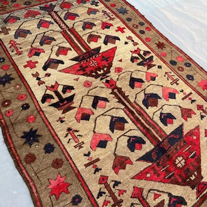 May include: A rectangular, hand-woven rug with a central design featuring red, brown, and navy blue geometric shapes on a tan background. The border is brown with floral and star patterns. The rug's design is symmetrical and detailed.