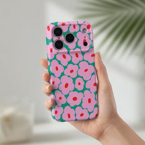 Peut inclure: Coque de téléphone rose avec un motif floral répété de fleurs roses à centres rouges sur fond vert. L'étui comporte des découpes pour l'appareil photo et les boutons du téléphone.