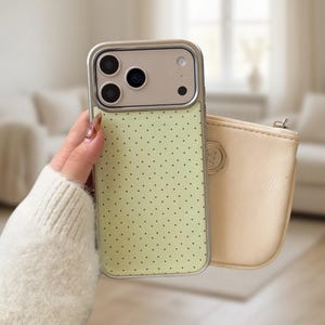 Könnte beinhalten: Eine hellgrüne iPhone-Hülle mit silbernem Rahmen und Polka-Dot-Muster. Eine kleine, cremefarbene Tasche mit Reißverschluss befindet sich neben der Handyhülle. Die Handyhülle hat drei Kameralinsen.