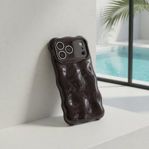 Pode incluir: Uma capa de telefone castanho escuro com um design texturizado e ondulado. A capa tem um acabamento brilhante e apresenta recortes para as lentes da câmera do telefone. A capa está encostada em uma parede branca, com uma piscina visível ao fundo.