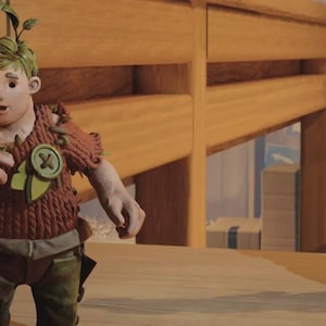 May include: Two handmade dolls, a male and a female, stand on a wooden surface. The male doll wears a brown knitted outfit with green accents and a leaf on his head. The female doll has blue hair and wears a yellow knitted top and blue jeans.