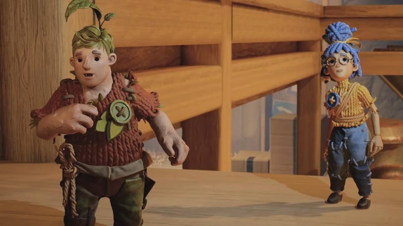 May include: Two handmade dolls, a male and a female, stand on a wooden surface. The male doll wears a brown knitted outfit with green accents and a leaf on his head. The female doll has blue hair and wears a yellow knitted top and blue jeans.