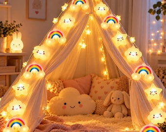 Può includere: Una catena di luci LED con forme alternate di nuvole sorridenti, arcobaleni colorati e stelle addormentate. Le luci emettono un bagliore caldo e sono drappeggiate su una tenda tipi in tessuto bianco, contenente un cuscino a nuvola e un coniglio.
