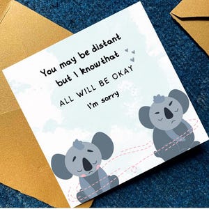 May include: A greeting card with a light blue background and the text "You may be distant but I know that ALL WILL BE OKAY I'm sorry". The card features two cartoon koalas and a gold envelope.