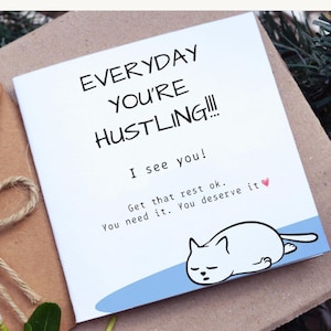 May include: A white greeting card with the text "EVERYDAY YOU'RE HUSTLING!!!" and "I see you!" A cartoon cat is drawn at the bottom. The card also says "Get that rest ok. You need it. You deserve it."