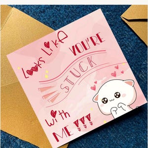 Puede incluir: Una tarjeta de felicitaci&oacute;n cuadrada con fondo rosa claro que muestra un gato blanco de dibujos animados con grandes ojos negros. El texto dice, Looks Like YOU'RE STUCK with ME !!!, junto a peque&ntilde;as ilustraciones de corazones rojos y estrellas.
