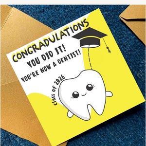 May include: A graduation card with the text "CONGRATULATIONS YOU DID IT! YOU'RE NOW A DENTIST!" features a cartoon tooth wearing a graduation cap. The card is yellow and white, with the words "class of 2026".