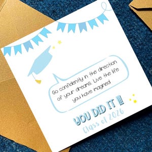 May include: A graduation card with a light blue mortarboard illustration and banner. The card reads "Go confidently in the direction of your dreams. Live the life you have imagined. YOU DID IT!! Class of 2026."