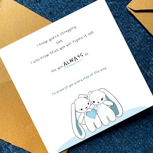 Peut inclure: Carte de v&oelig;ux blanche avec une bordure bleue et une illustration de deux lapins tenant un c&oelig;ur bleu. Le texte dit : &laquo; Je sais que tu as du mal, mais je sais aussi que tu vas t'en sortir comme tu le fais TOUJOURS. &raquo;