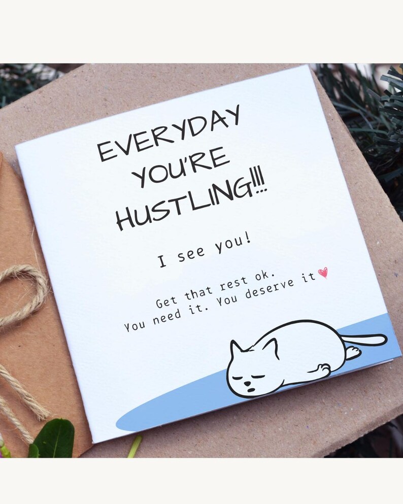 May include: A white greeting card with the text "EVERYDAY YOU'RE HUSTLING!!!" and "I see you!" A cartoon cat is drawn at the bottom. The card also says "Get that rest ok. You need it. You deserve it."
