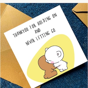 May include: A greeting card with the text "THANKYOU FOR HOLDING ON AND NEVER LETTING GO". The card features a cartoon illustration of two bear-like characters hugging on a yellow background.