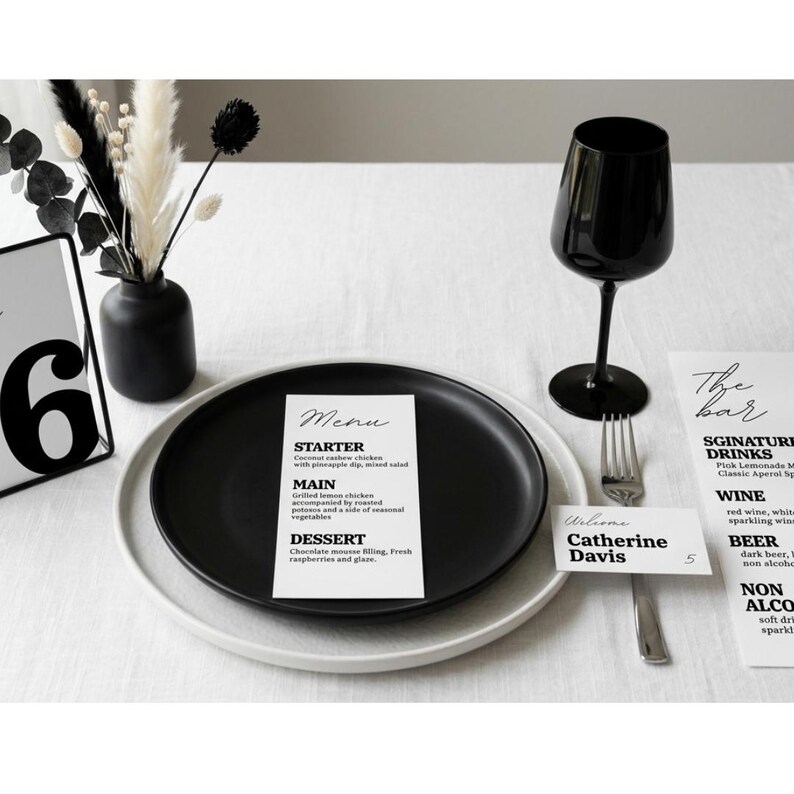 Op de afbeelding: Een minimalistische tafelsetting met een zwart bord, een wijnglas en een menukaart. De menukaart geeft een voorgerecht, hoofdgerecht en dessert weer. Een naambordje luidt "Catherine Davis".