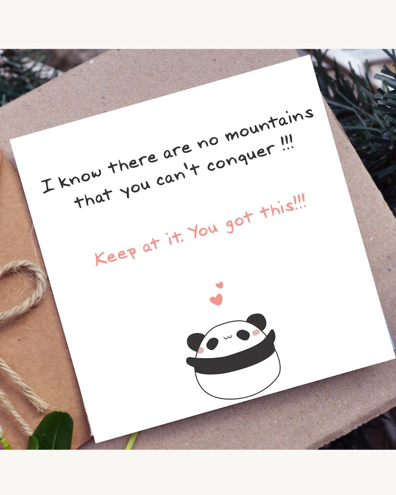 May include: A white greeting card with the text "I know there are no mountains that you can't conquer !!! Keep at it. You got this!!!" and a cartoon panda bear illustration. The card is on a brown surface.