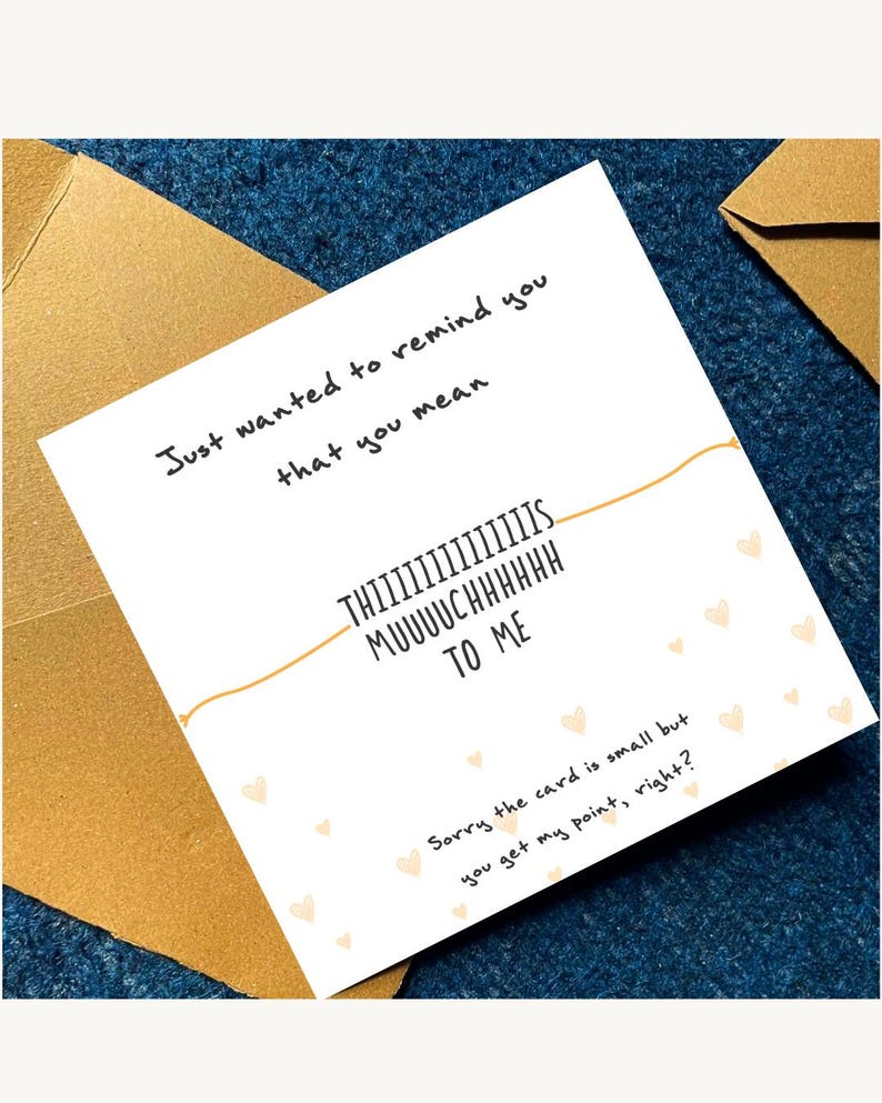 Puede incluir: Una tarjeta blanca con el texto "Just wanted to remind you that you mean THIIIIIIIIIIIIIIS MUUUUCHHHHHH TO ME". La tarjeta est&aacute; decorada con peque&ntilde;as formas de coraz&oacute;n y est&aacute; colocada sobre una superficie azul con un sobre dorado.